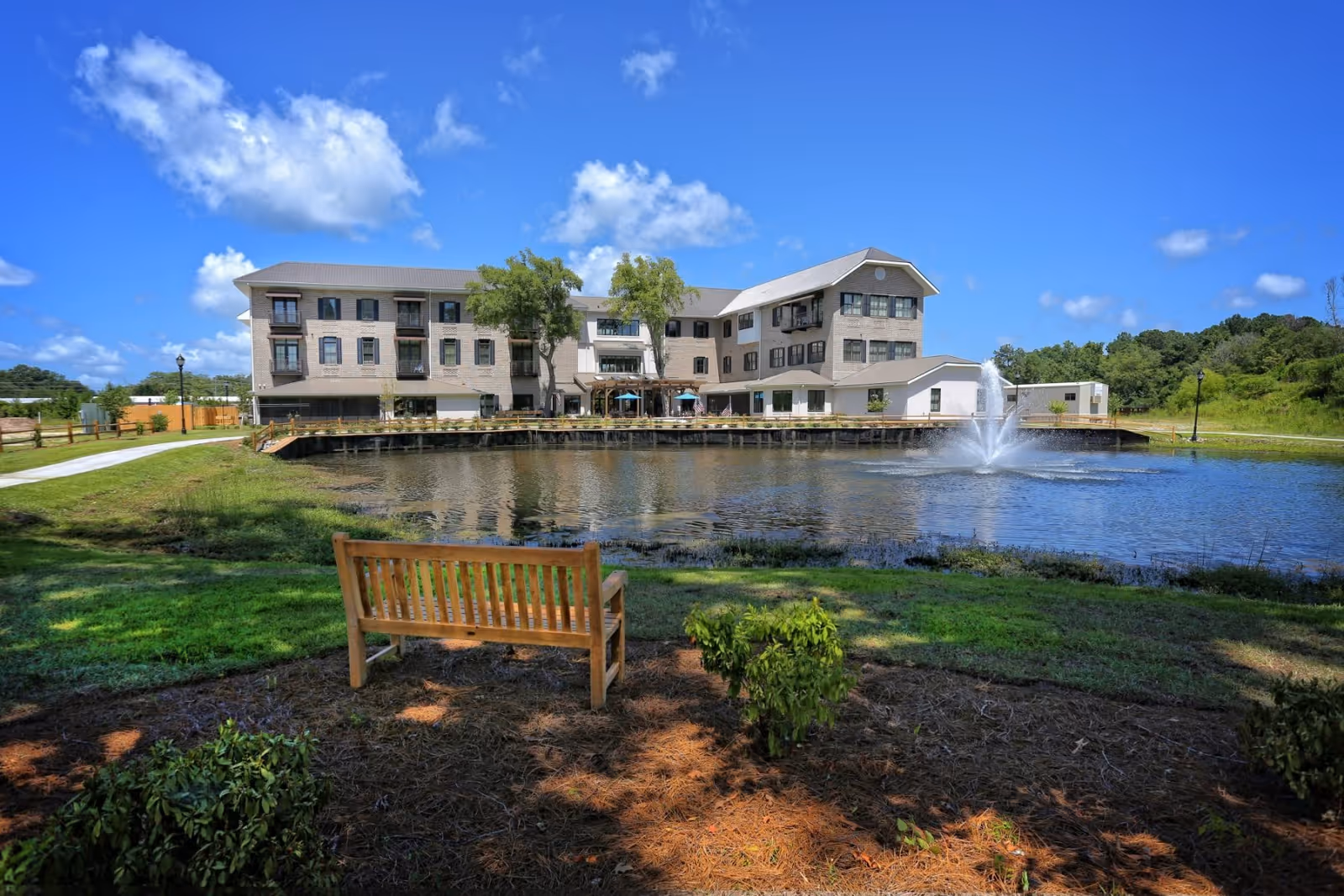 Exterior view of The Suites at Station Exchange with a pond, fountain, and bench.