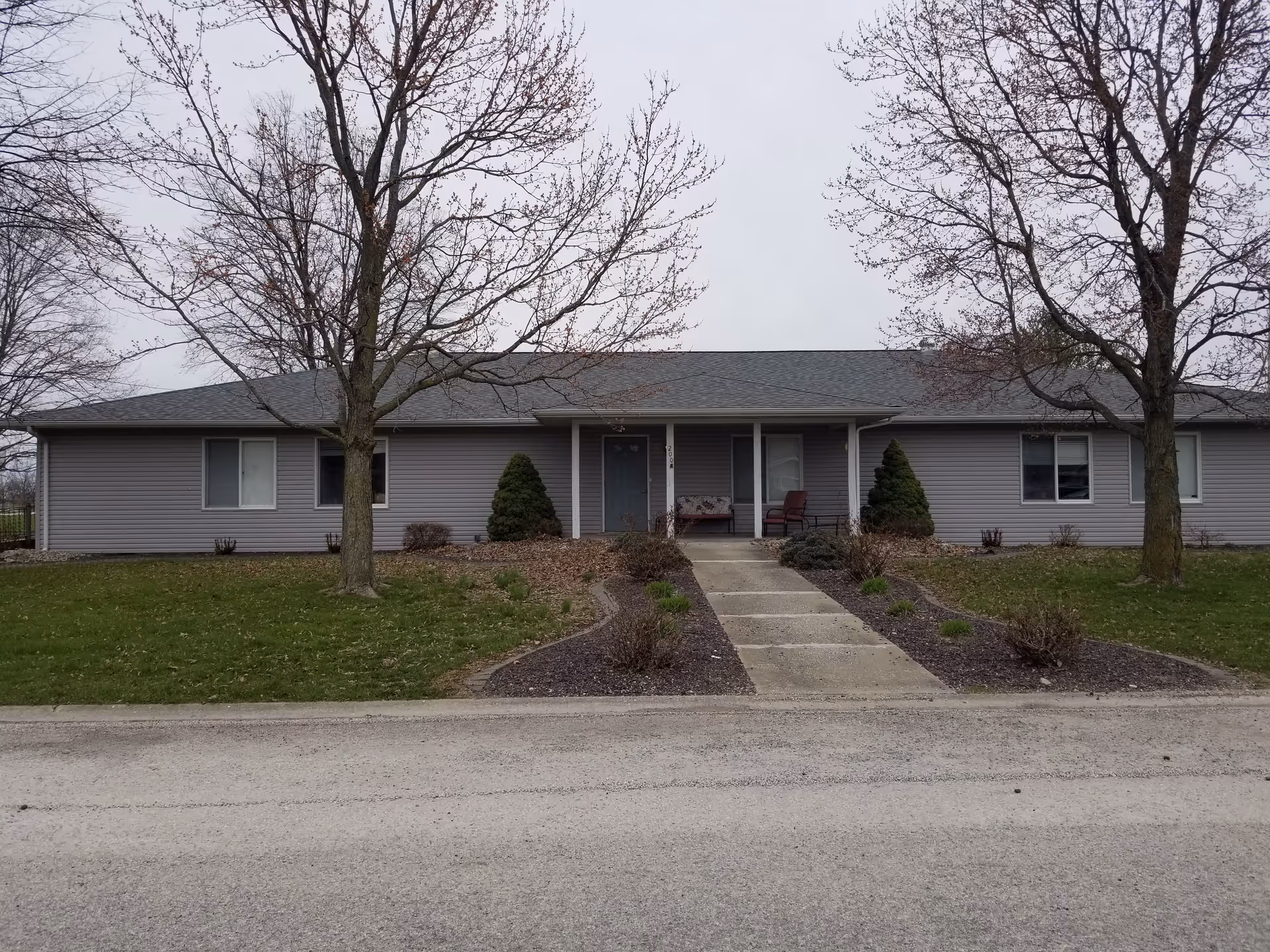 Single-story gray senior living facility exterior with a front entrance and bare trees.