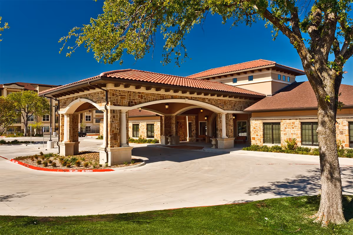 Front view of a stone-clad senior living facility entrance with a covered drive-through and trees.