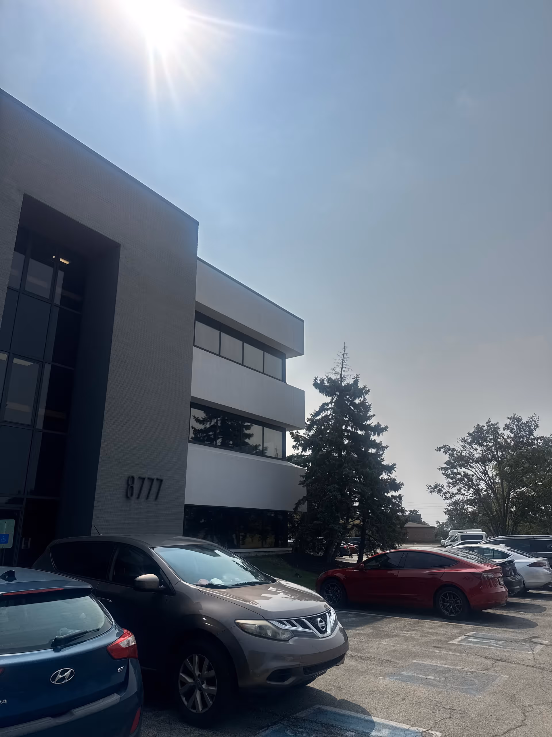 Modern multi-story building with several parked cars and a bright sunny sky.