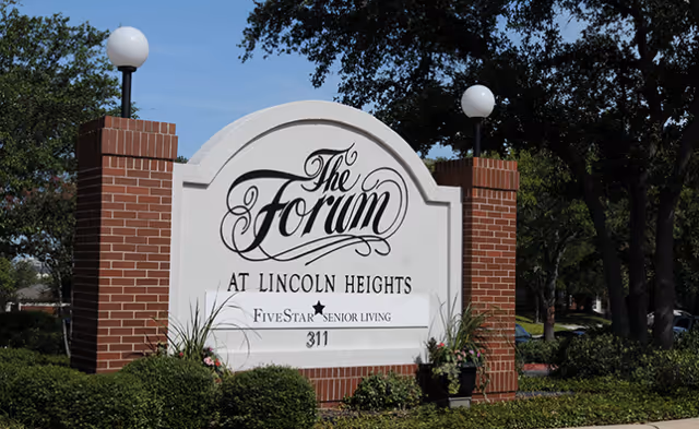 Entrance sign reading "The Forum at Lincoln Heights" mounted between brick pillars with globe lamps and landscaping.