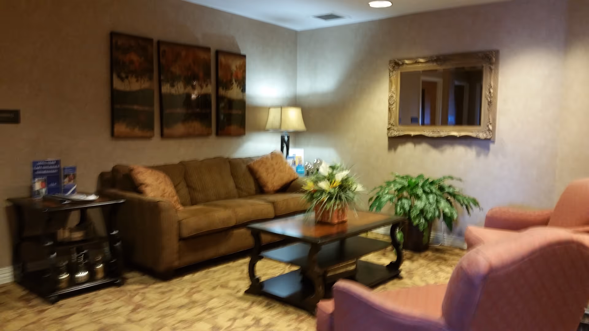 Cozy hotel-style living room with sofa, coffee table, lamp, plants, and wall art.