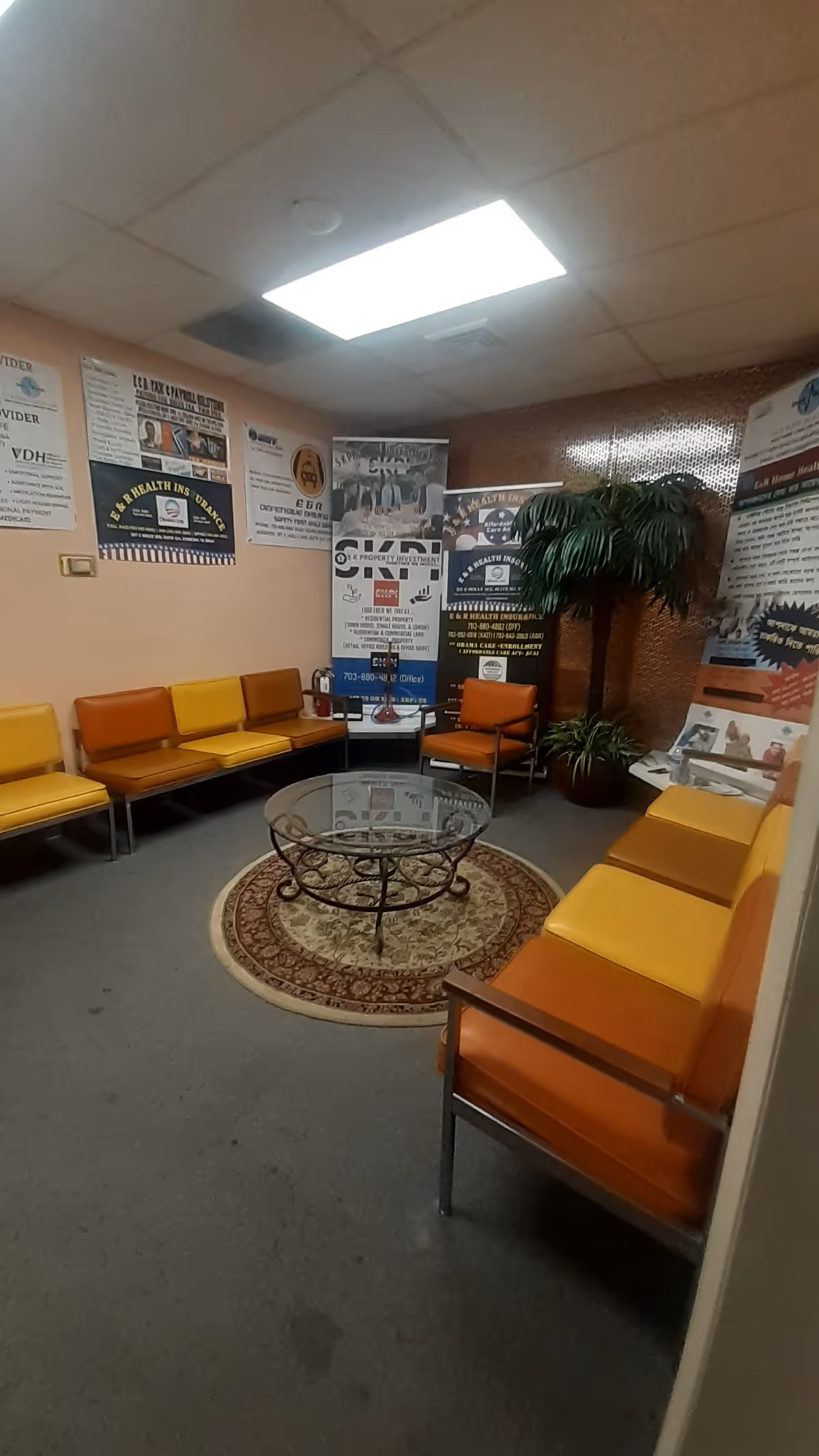 Waiting area with orange chairs around a glass coffee table and posters.