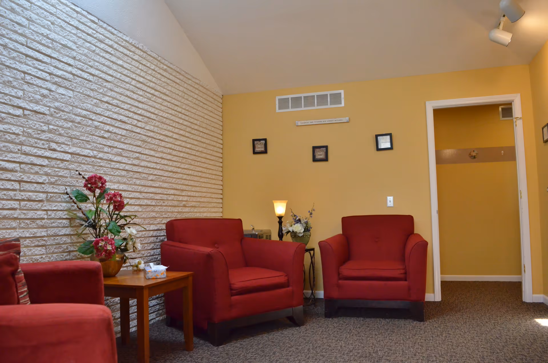 A cozy waiting area with red armchairs, a small table with flowers, and yellow walls.
