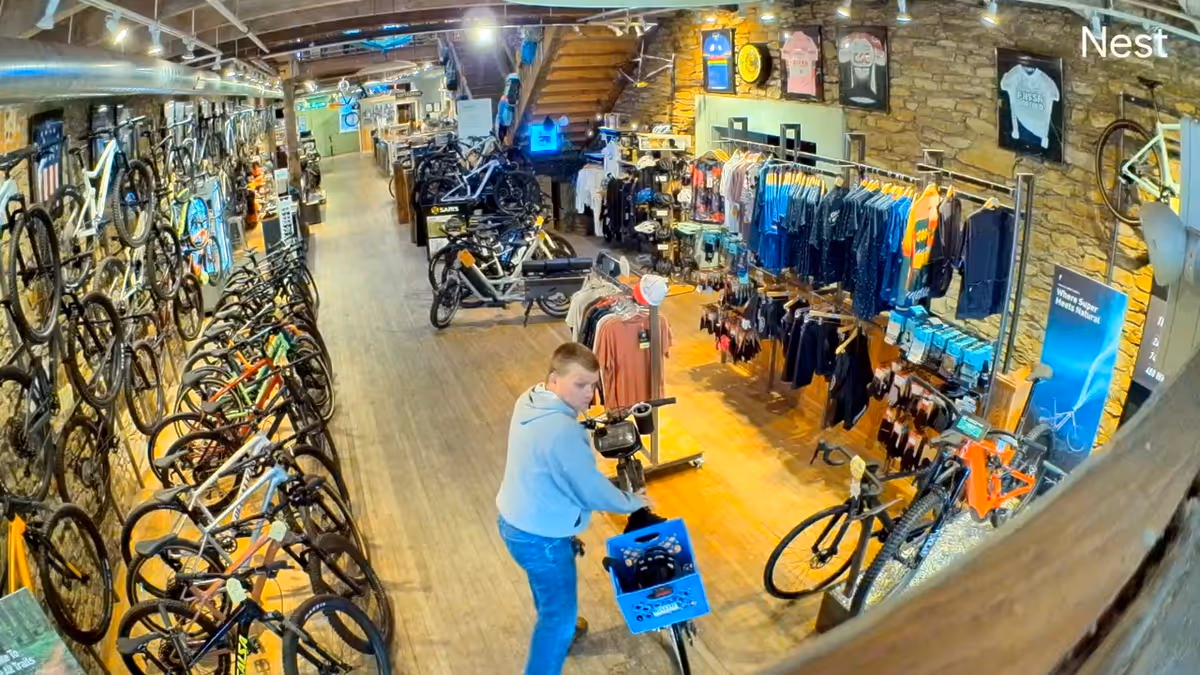 A bicycle shop interior with bikes on walls and racks, and a shopper in the center.