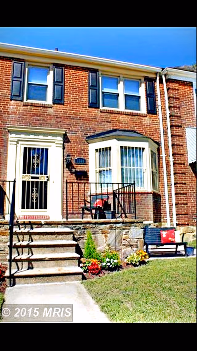 Brick townhouse-style front entrance with stairs, railing, and porch seating.