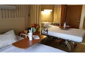 Two hospital-style beds in a shared rehab room with side tables and flowers
