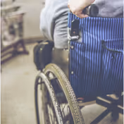 Close-up of a wheelchair and a person in blue striped clothing indoors.