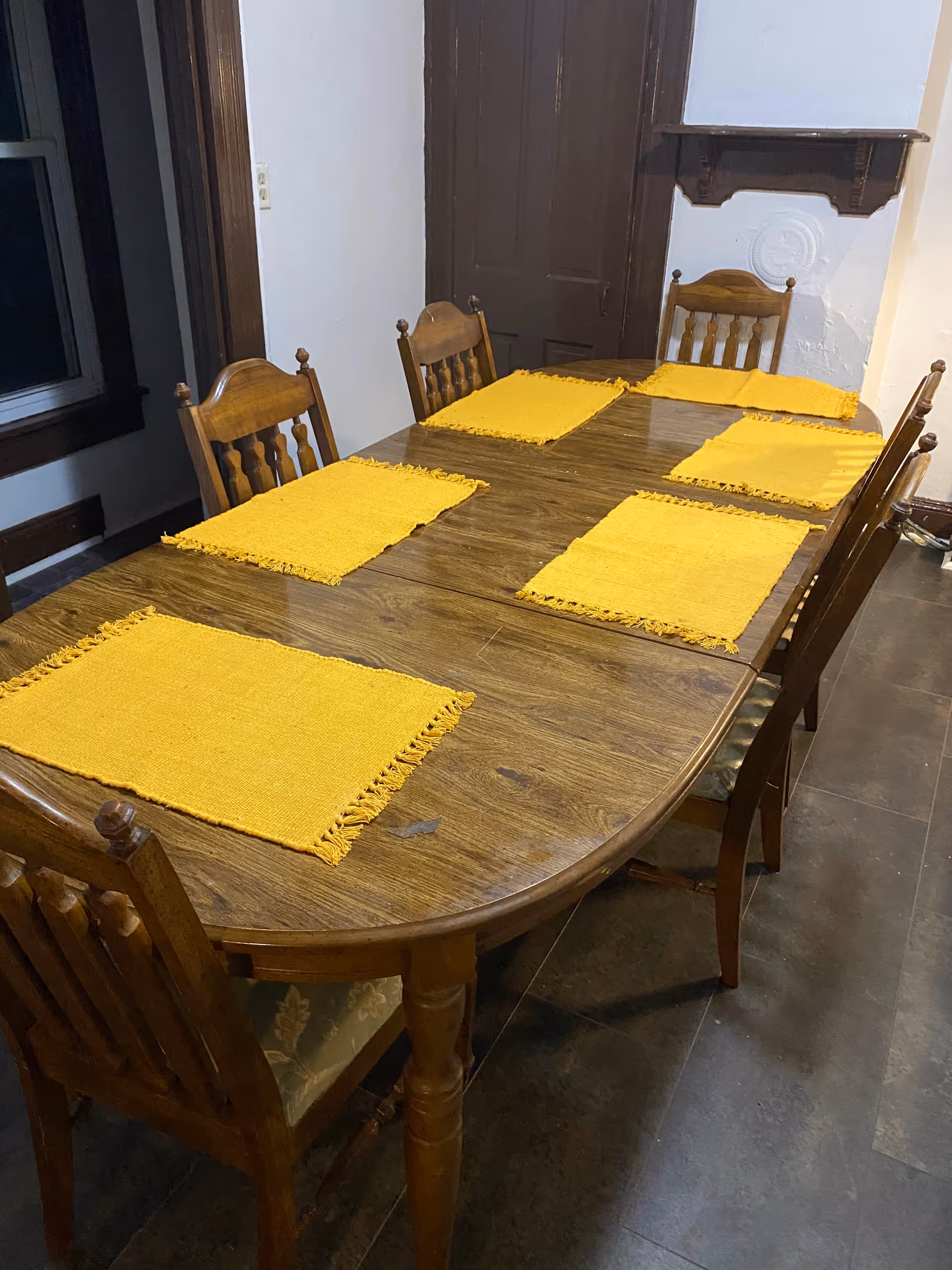A wooden dining table with six yellow placemats in a dining room.