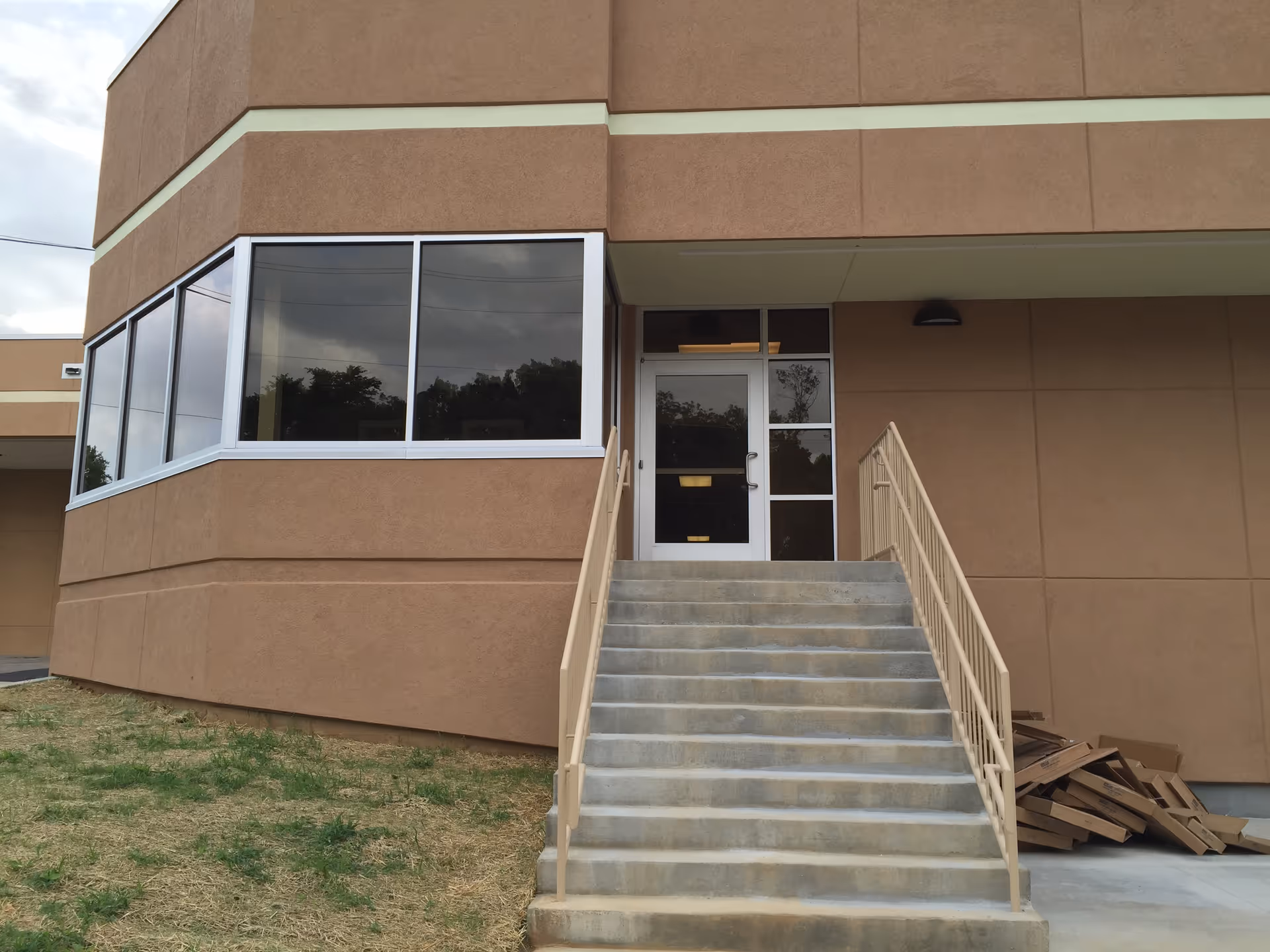 Exterior view of a tan building with large windows and a concrete staircase to entrance.