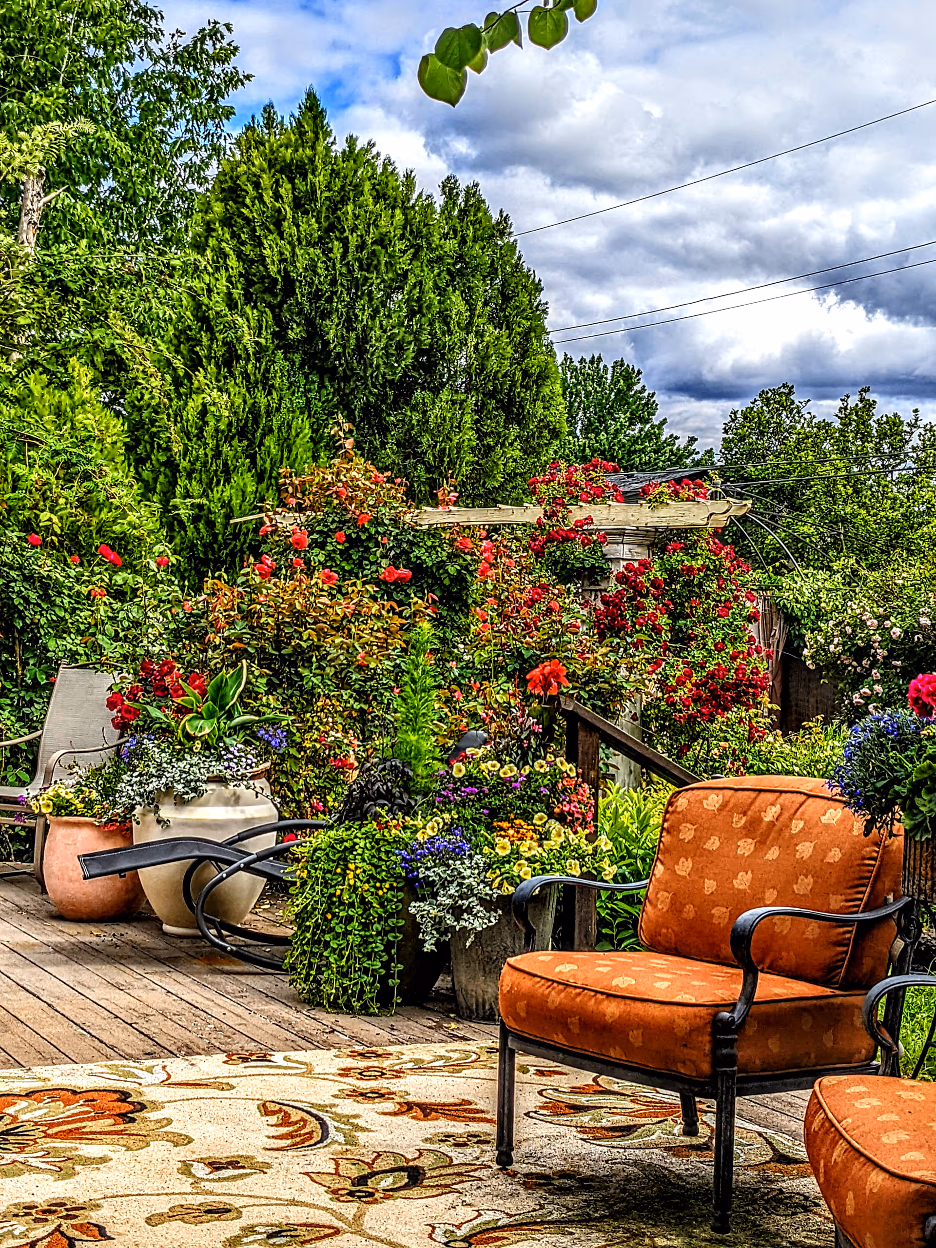 Colorful garden patio with potted flowers, wooden deck, and cushioned seating.