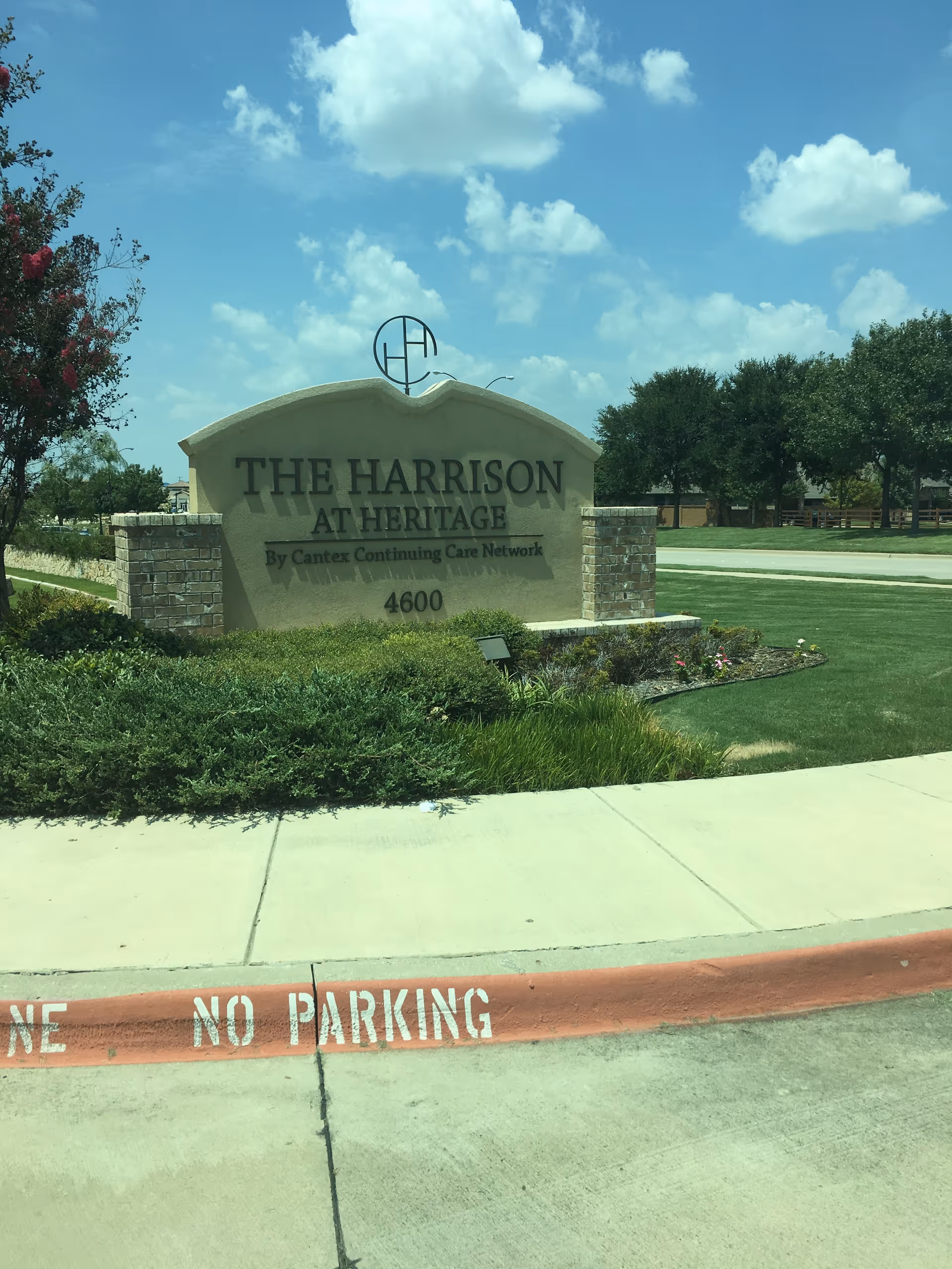 Exterior view of The Harrison at Heritage sign with landscaping and a no-parking curb.