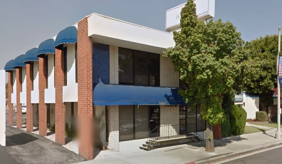 Exterior view of a two-story brick building with blue awnings and trees.