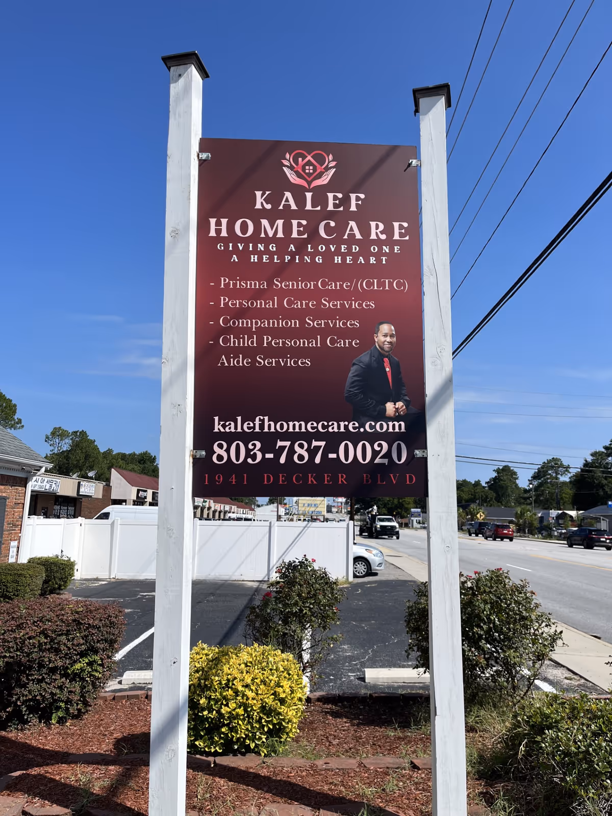 Tall KALEF Home Care sign displayed on two white posts by a road.