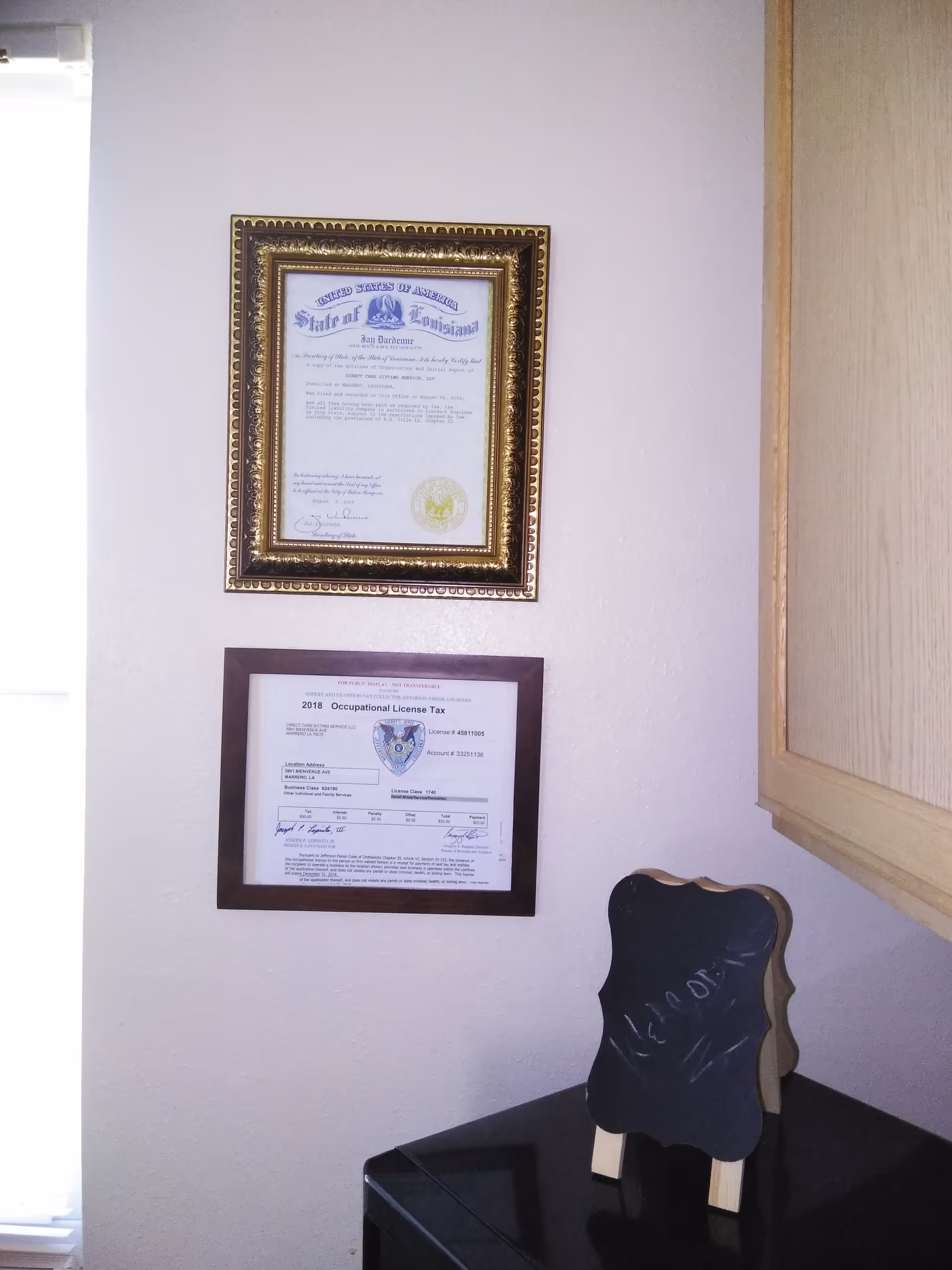 Two framed certificates hang on a light colored wall beside a cabinet with a chalkboard sign.