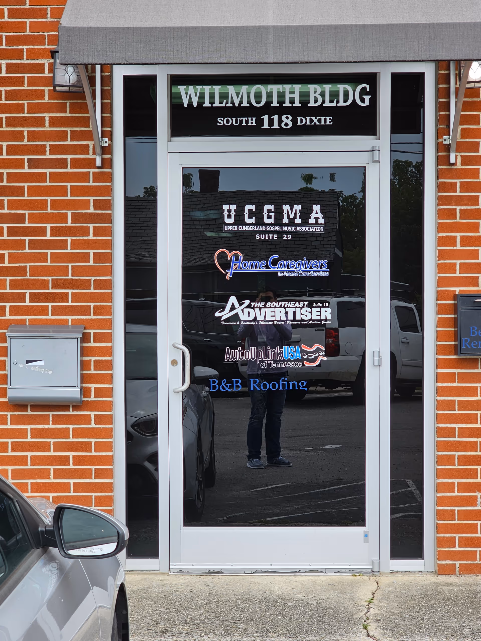 Brick building exterior with a glass doorway displaying multiple business logos.