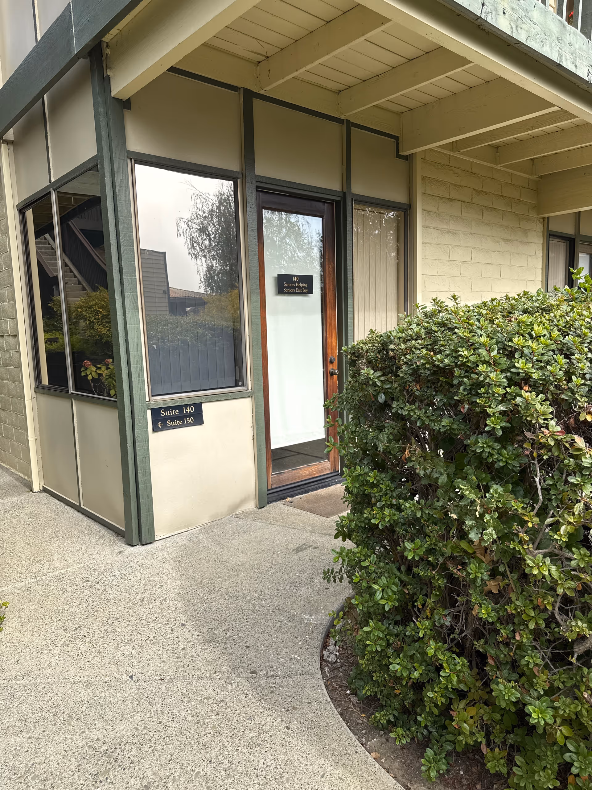 Exterior view of a senior living facility entrance with glass door and shrubs.
