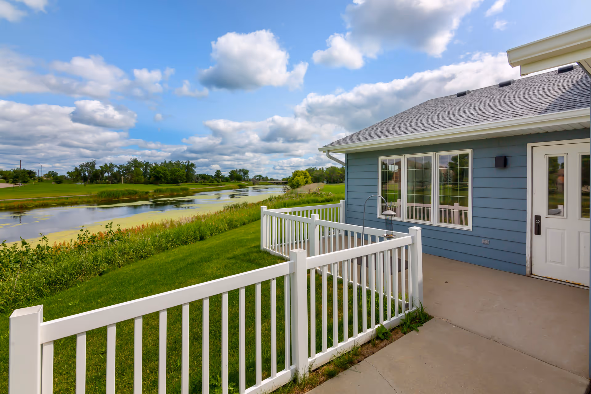 Blue senior living home exterior with white railing and river view.
