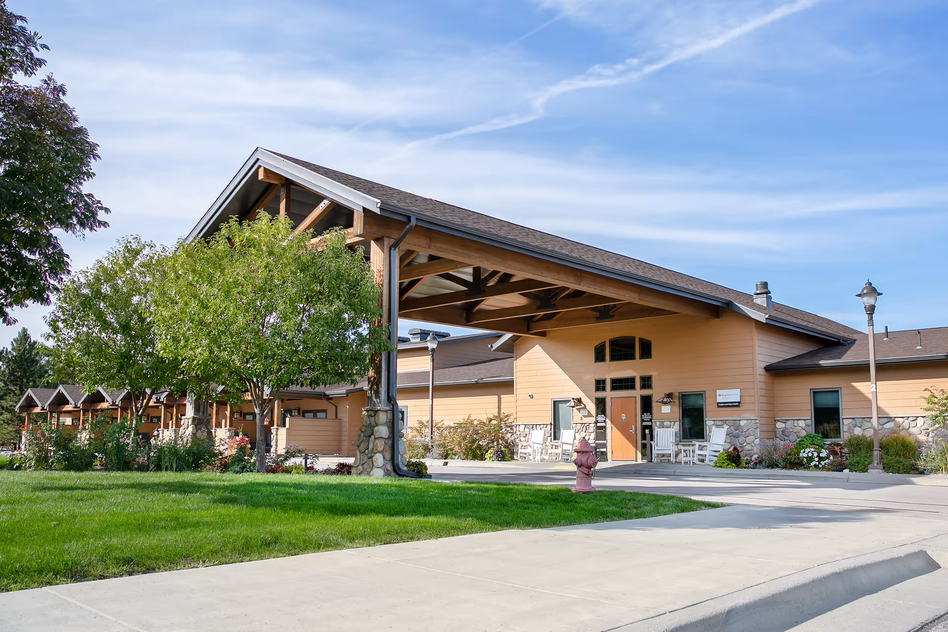 Sunny entrance to Monument Health Home+ Home Health and Hospice building with a covered portico.