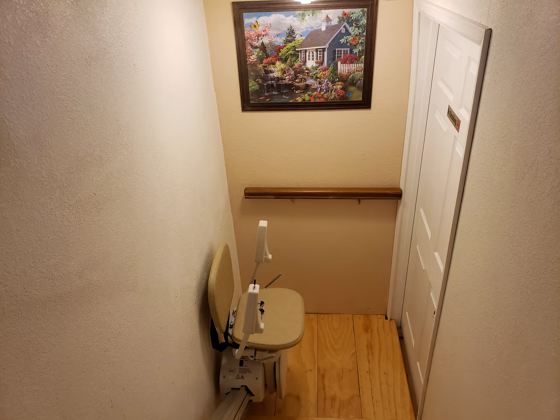 Narrow hallway with a beige mobility chair and framed landscape painting.