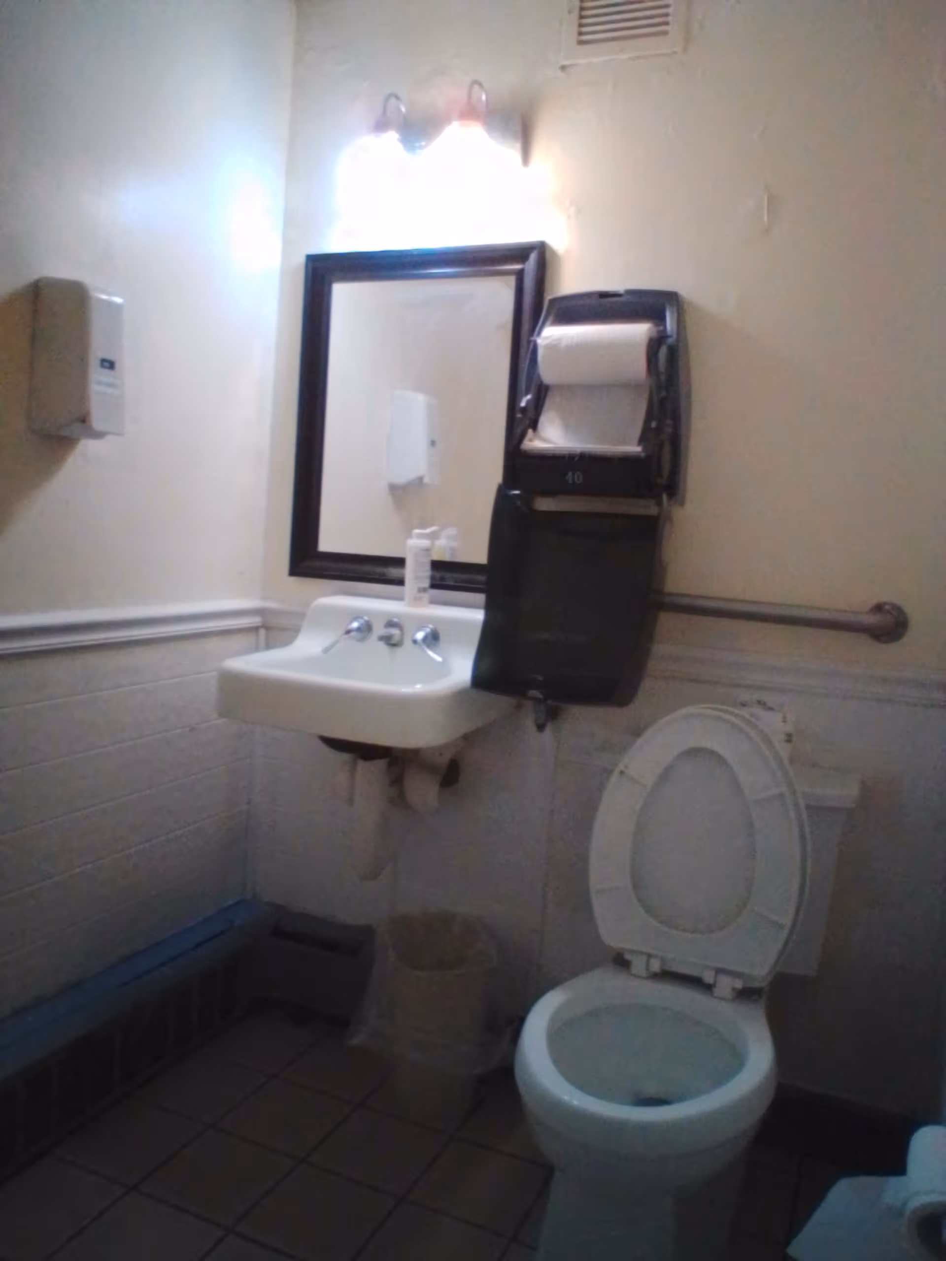 Compact bathroom with sink, mirror, paper towel dispenser, and toilet.