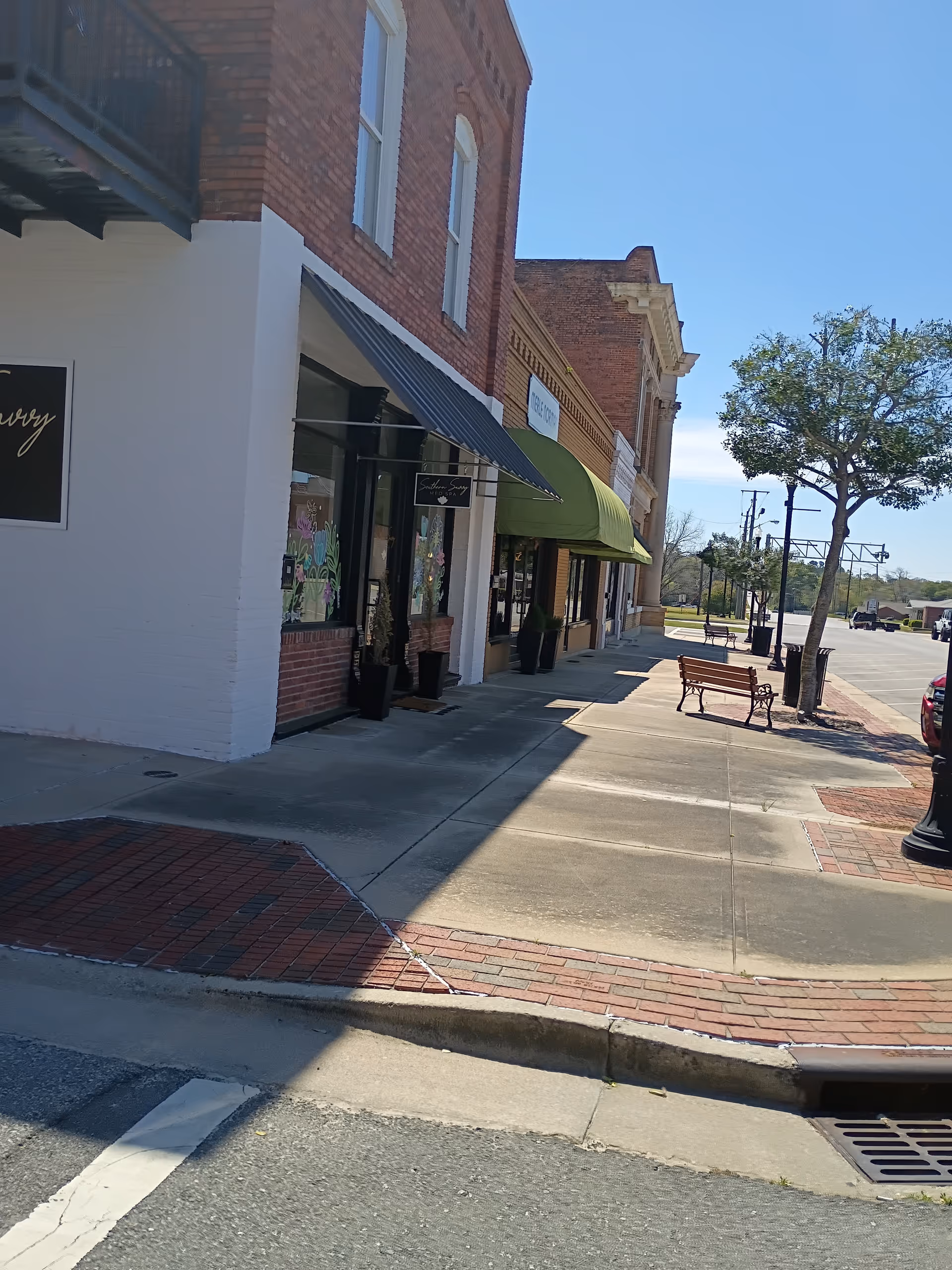 Row of brick storefronts along a sunny sidewalk with awnings.