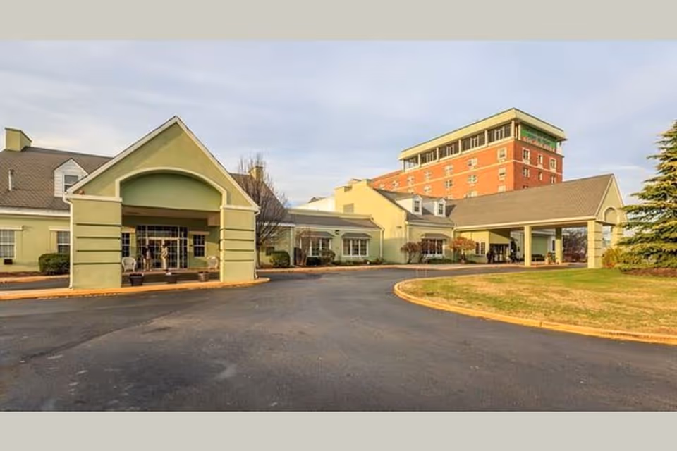 Front exterior of a multi-story senior living facility with a covered porte-cochère and circular driveway.