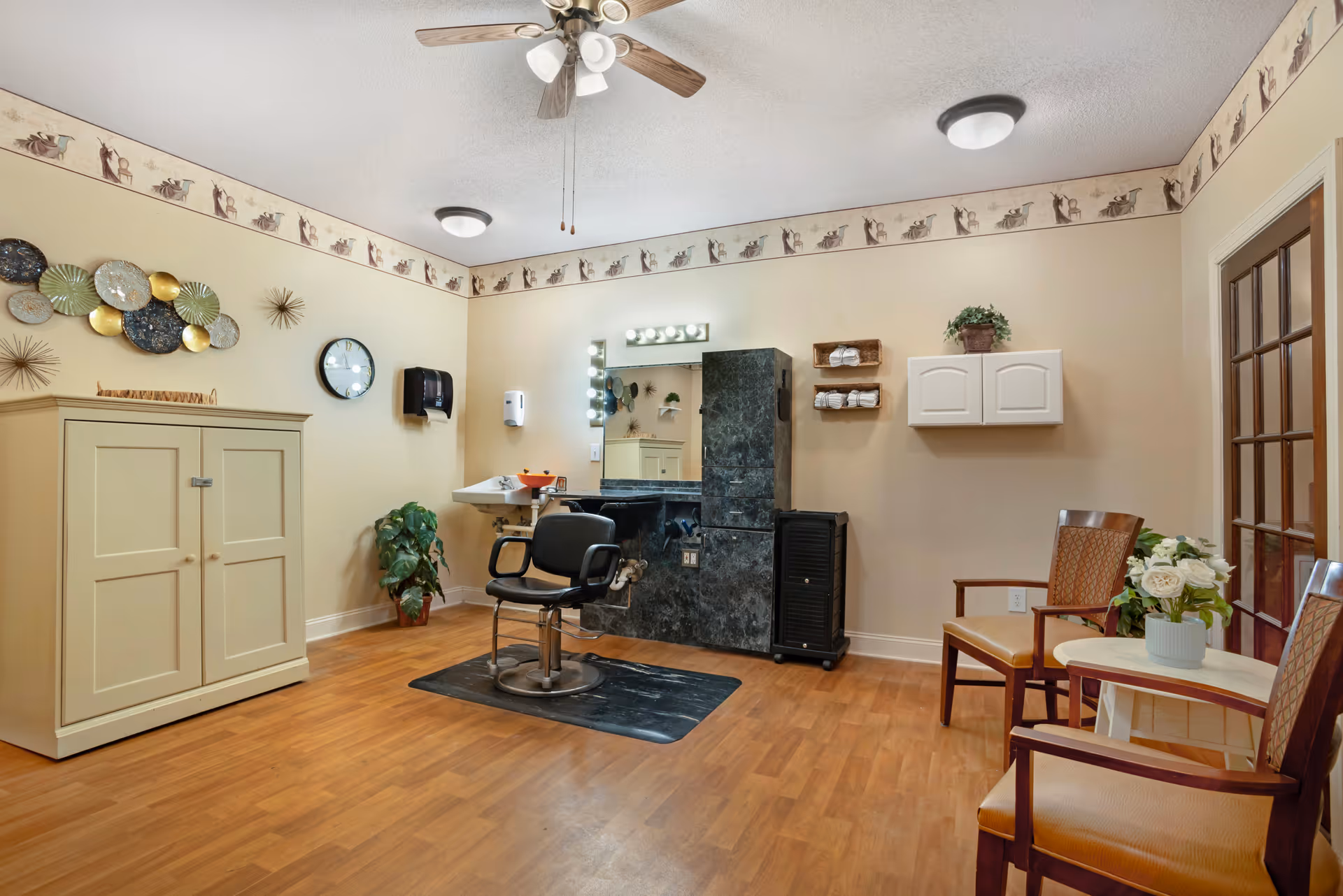 Hair salon in a senior living facility featuring a chair, mirror, sink, and cabinets.