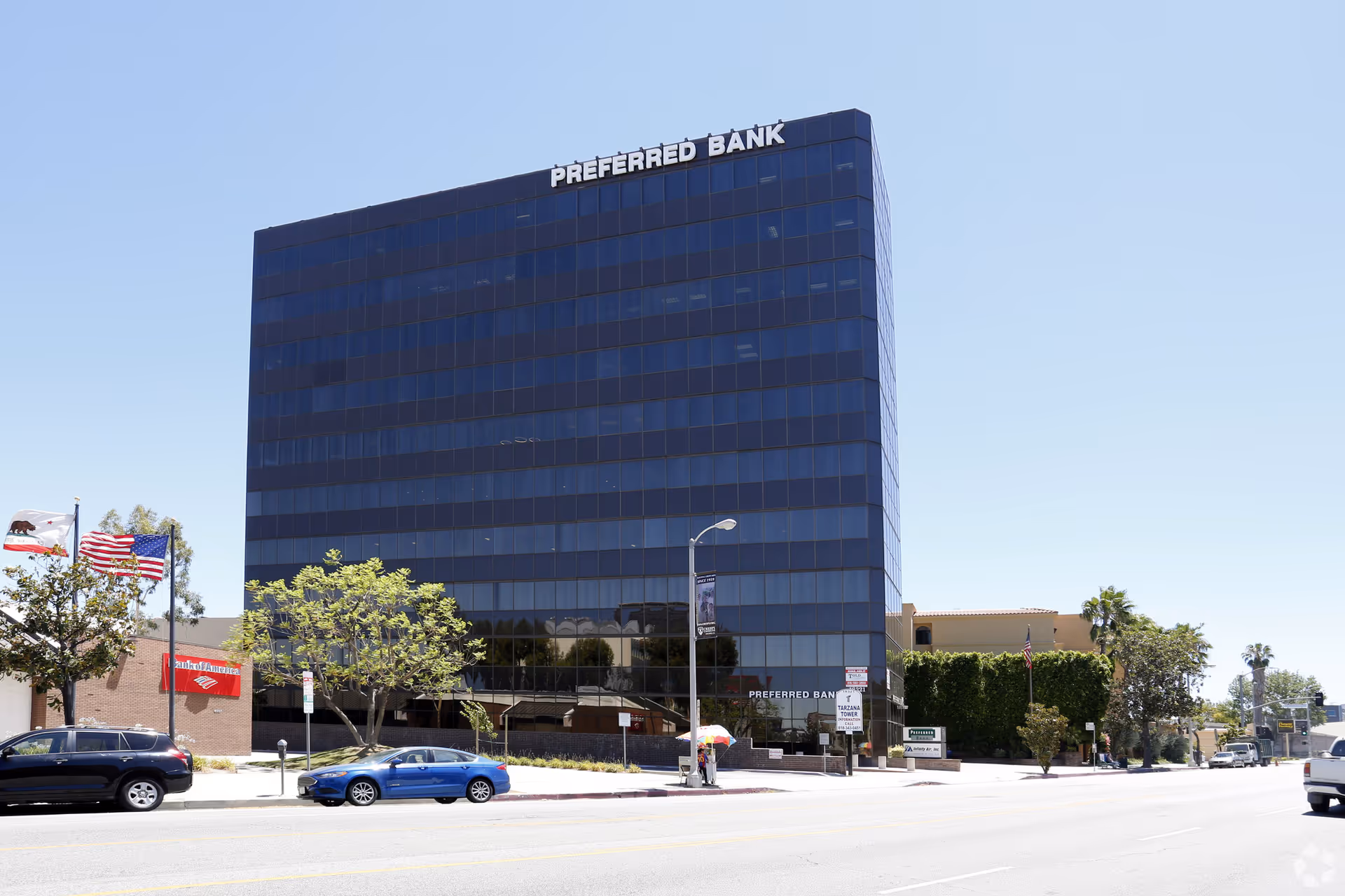 Tall glass-fronted office building with a Preferred Bank sign along a city street.