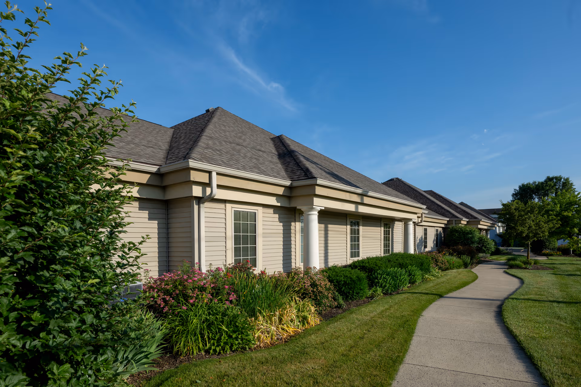 Row of beige, single-story facility buildings with a curved walkway and manicured landscaping.
