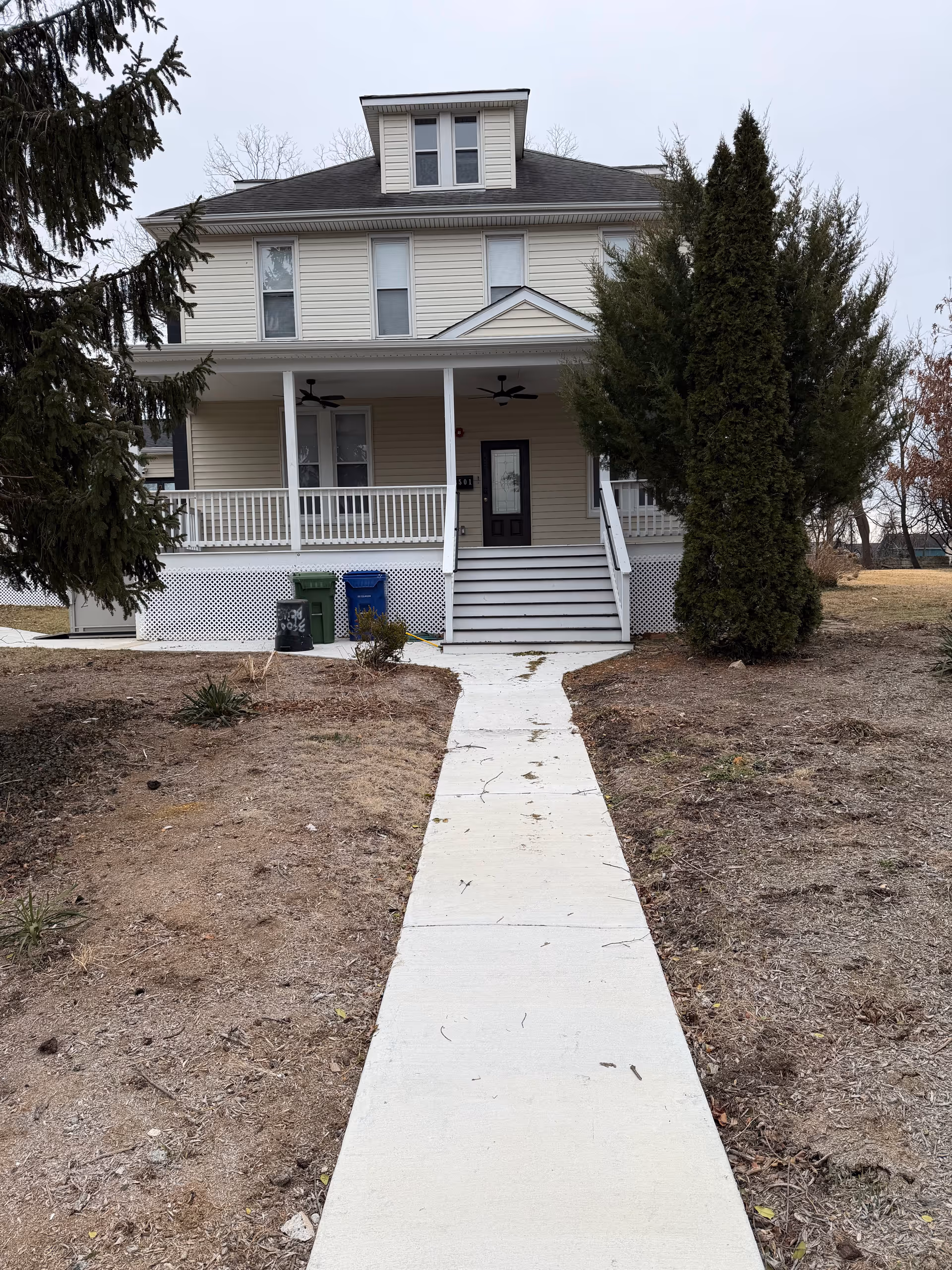 Two-story beige house with a front porch, railing, stairs, and a central walkway.