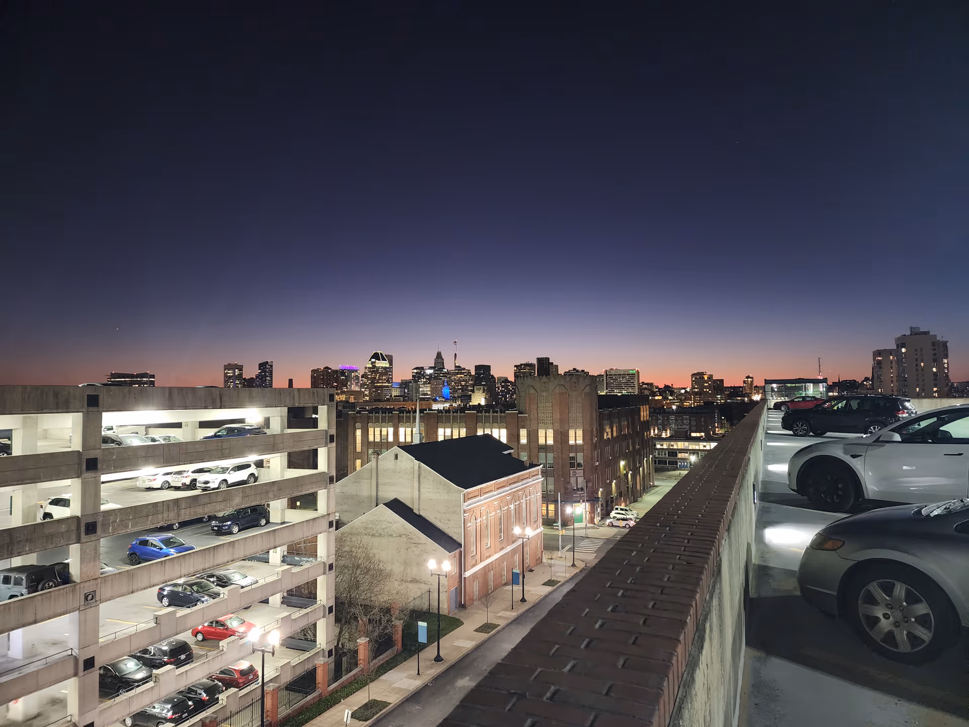 Dusk city skyline visible from a rooftop parking structure.