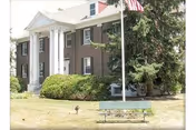 Hazel L. Carpenter Adult Home front, brick building with white columns, flag, and bench.
