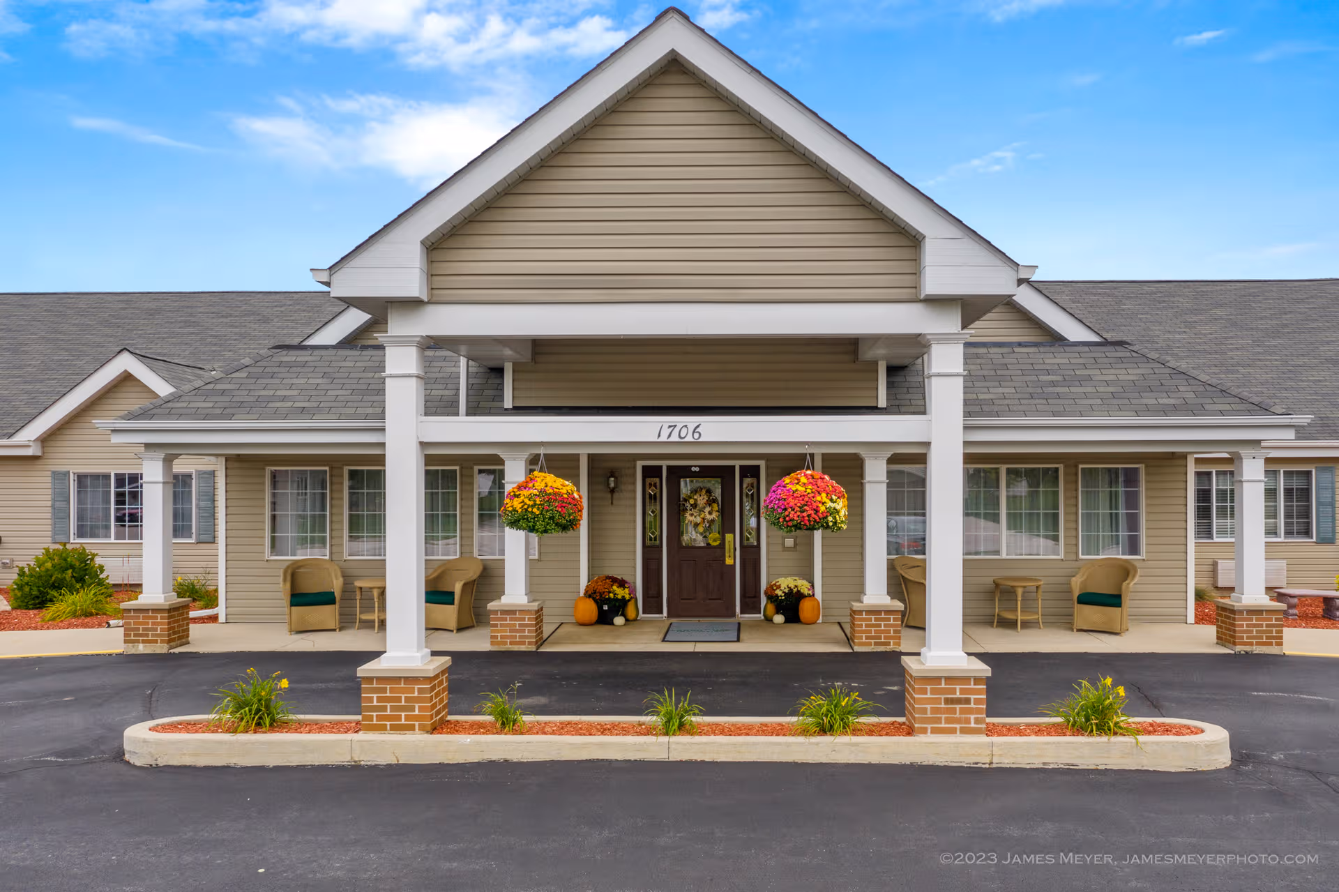 Front entrance of LakeHouse New Holstein senior living facility with hanging baskets and pumpkins.