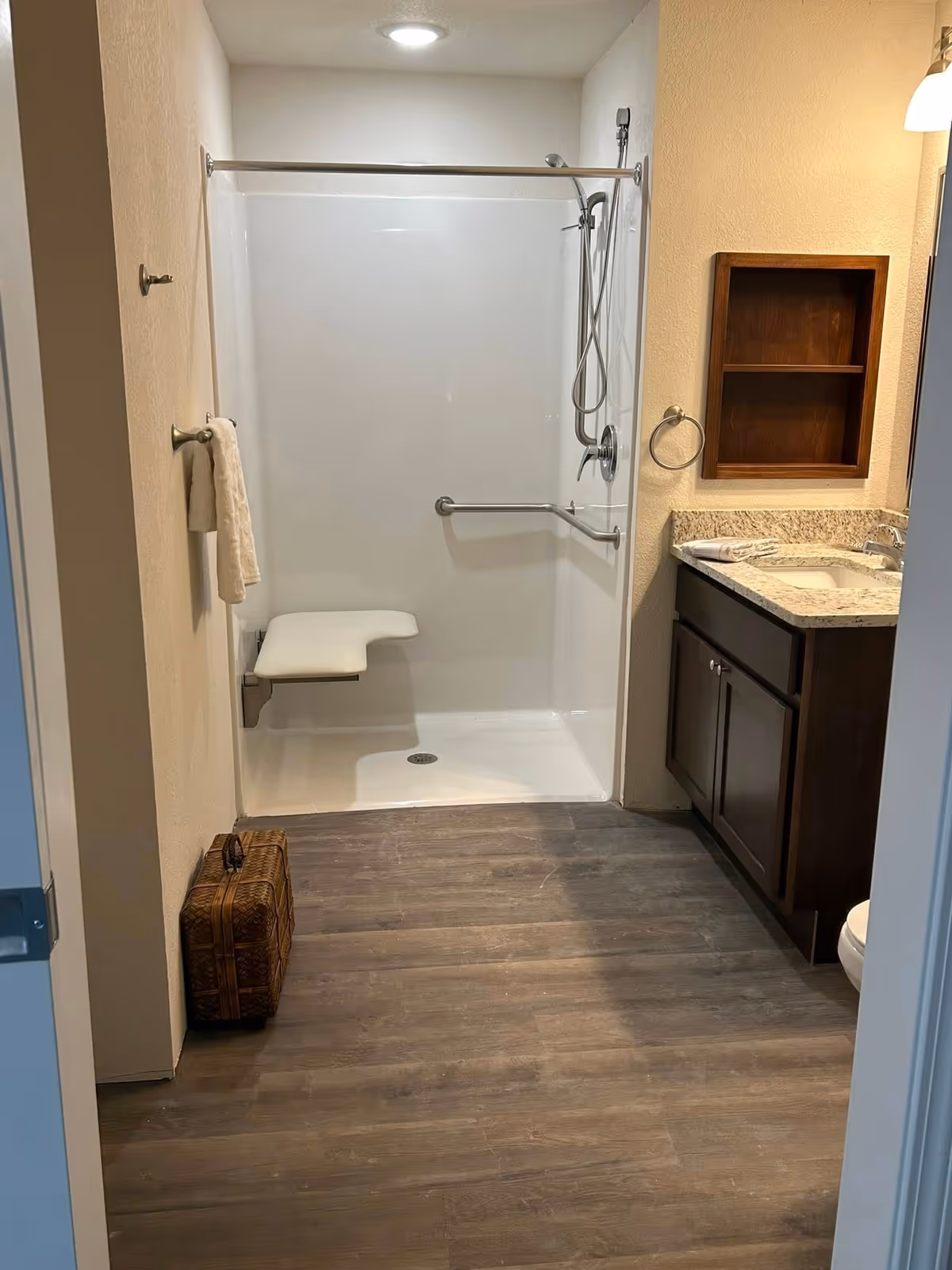 Accessible bathroom with a white walk-in shower, bench, and dark vanity.