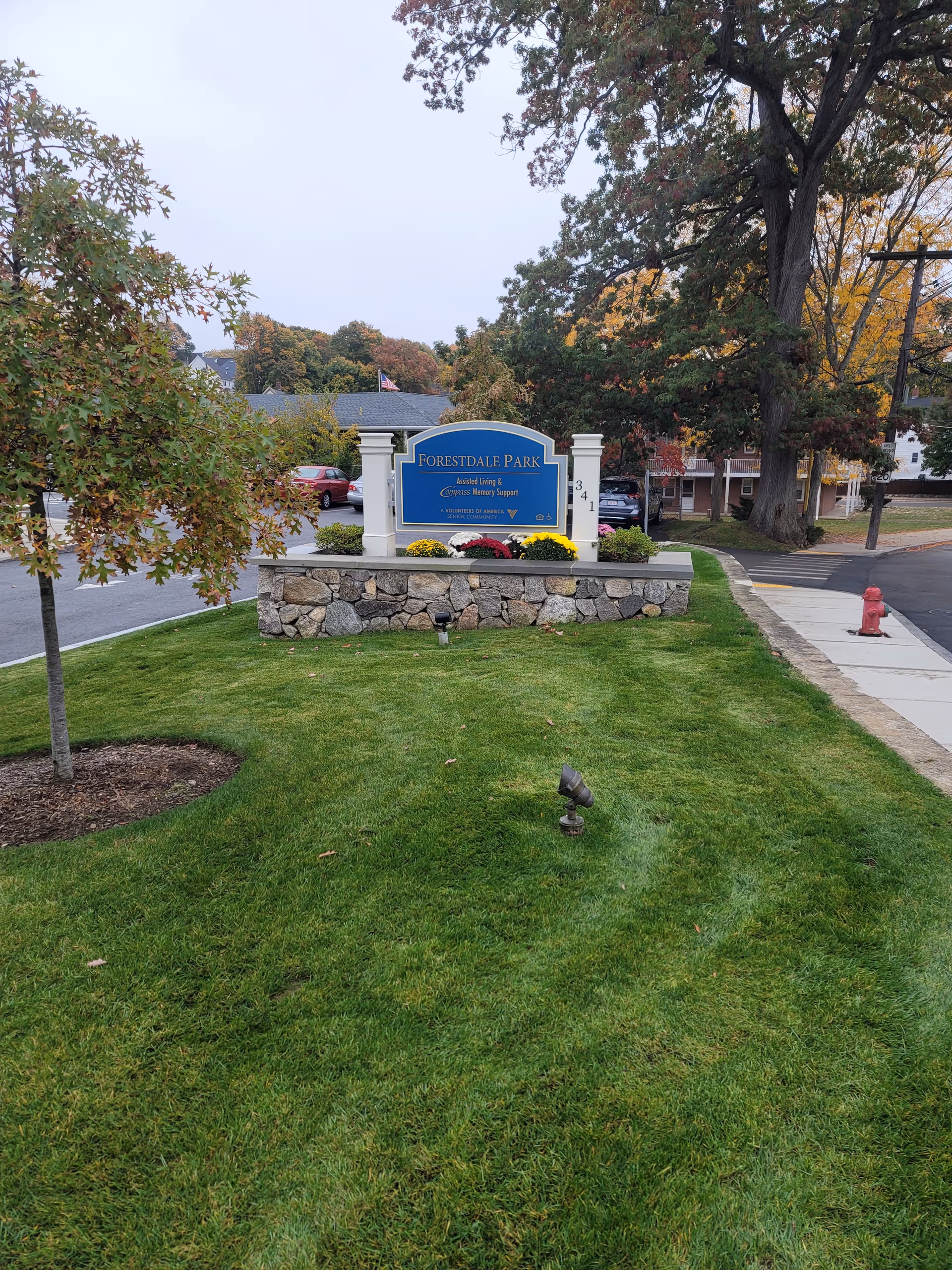 Forestdale Park Senior Living sign on a stone base amid green lawn and trees.