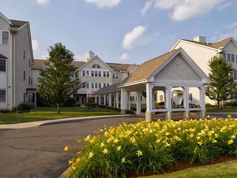 Senior living facility exterior with a covered entrance and yellow flowers in the foreground.