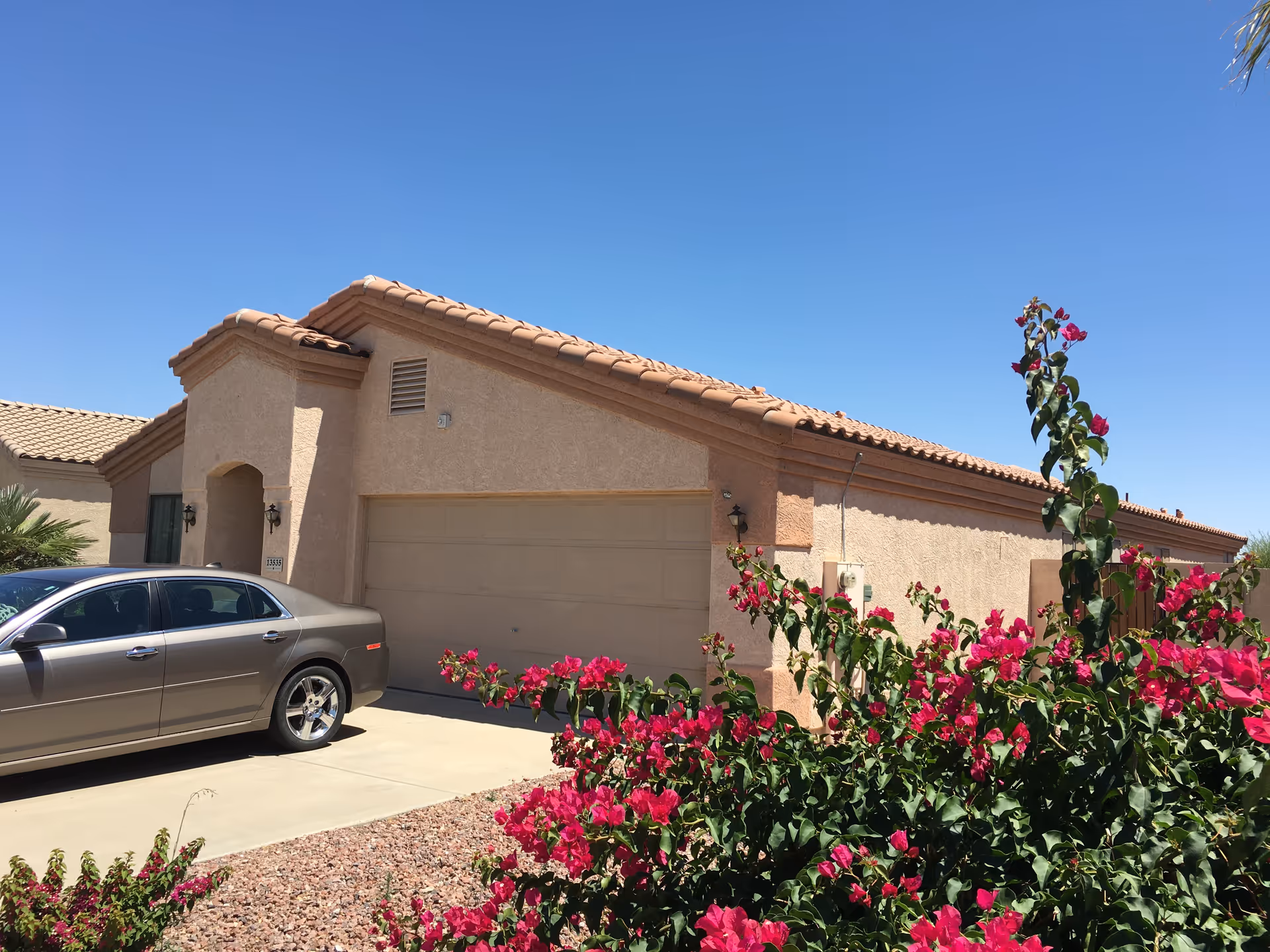 Exterior view of Desert Palms Adult Care Home with a car and pink flowers.