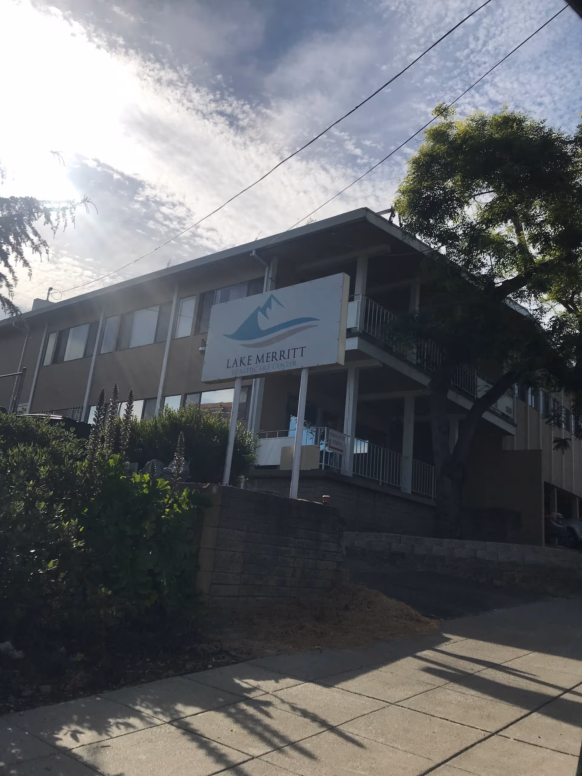 Front exterior of a two-story Lake Merritt Healthcare Center with a sign and trees.