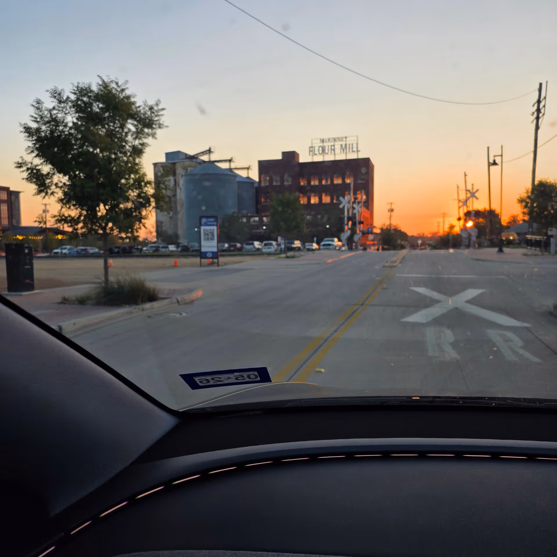 Sunset view of a street with a brick mill building and railroad tracks ahead.