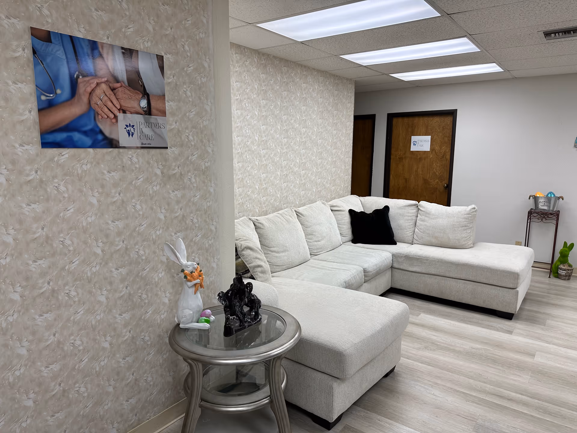 Cozy lounge in a senior care facility with a light gray sectional sofa and wall poster.