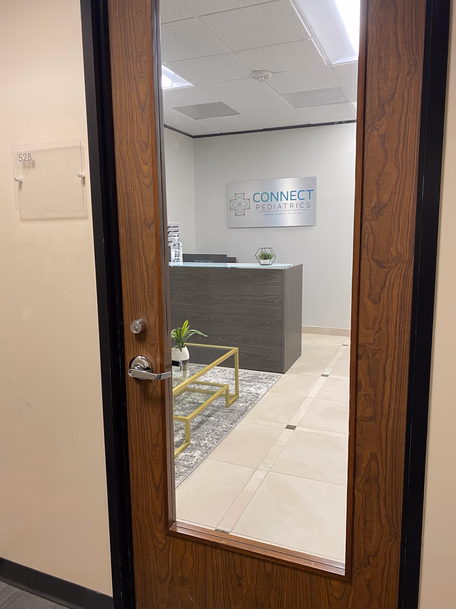 Reception area viewed through doorway with desk, plants, and Connect Pediatrics sign.