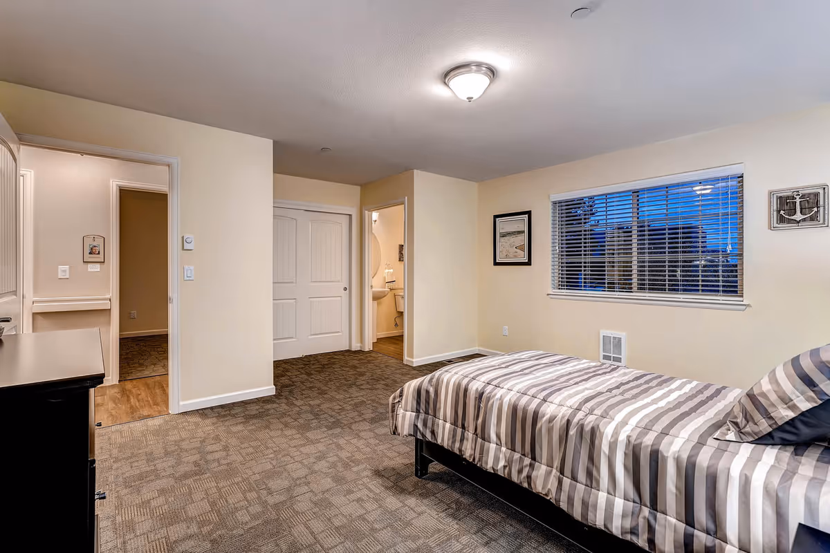 Bedroom in Rocky Mountain Assisted Living Quincy West with striped bed and window.