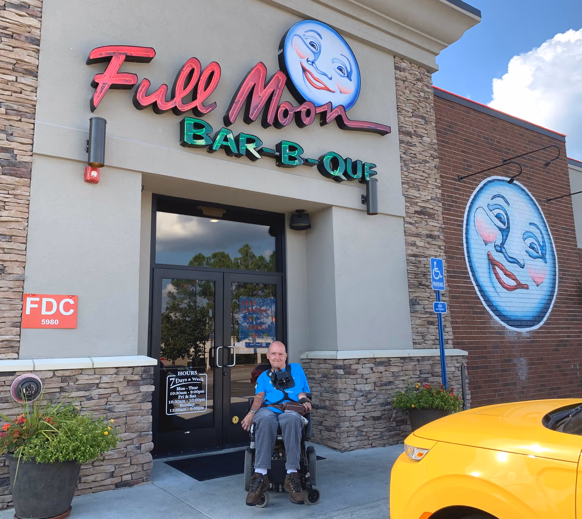 A man in a wheelchair sits outside the Full Moon Bar-B-Que entrance.