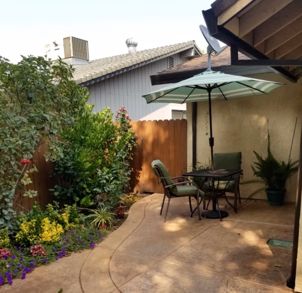 A small outdoor patio with a table, chairs, umbrella, and potted plants along a fence
