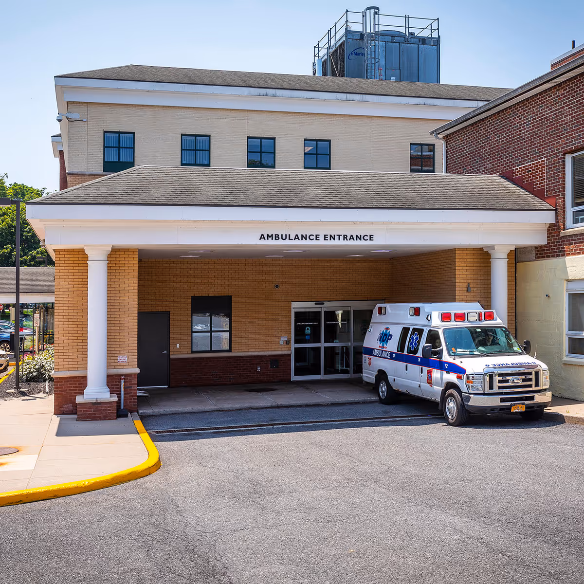 Ambulance parked at the front entrance of a brick hospital building.