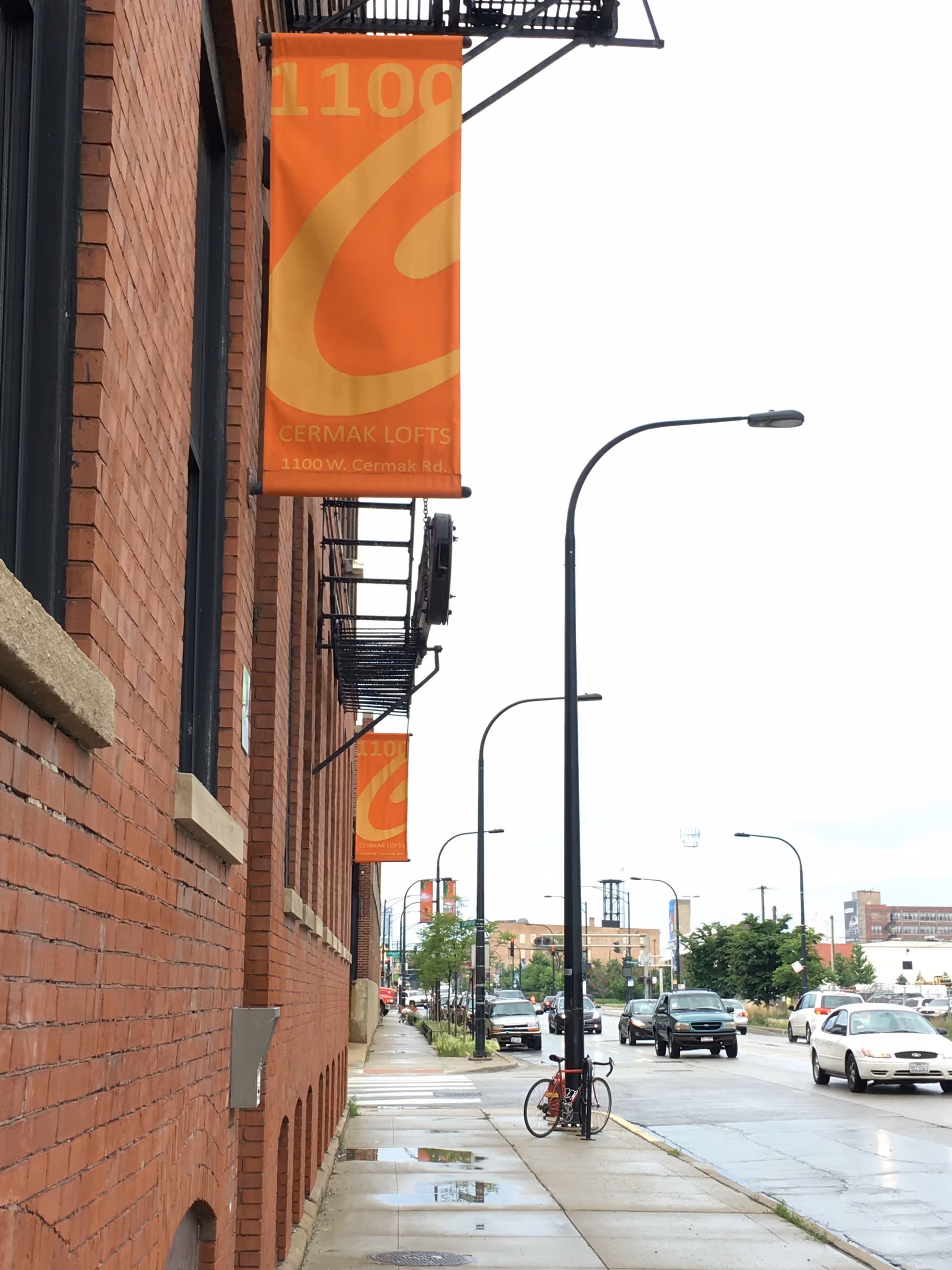 Brick apartment building along a city street with orange banners and parked cars.