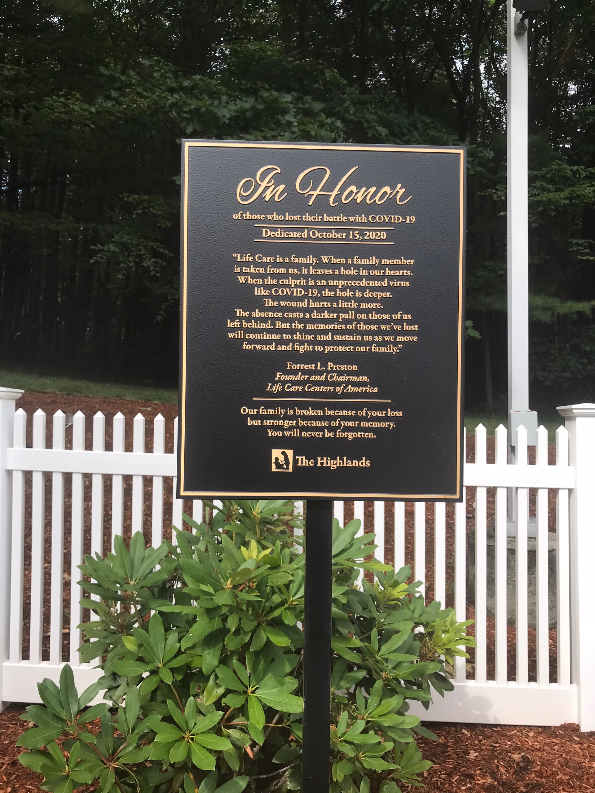 In Honor plaque on a post in front of a white picket fence.