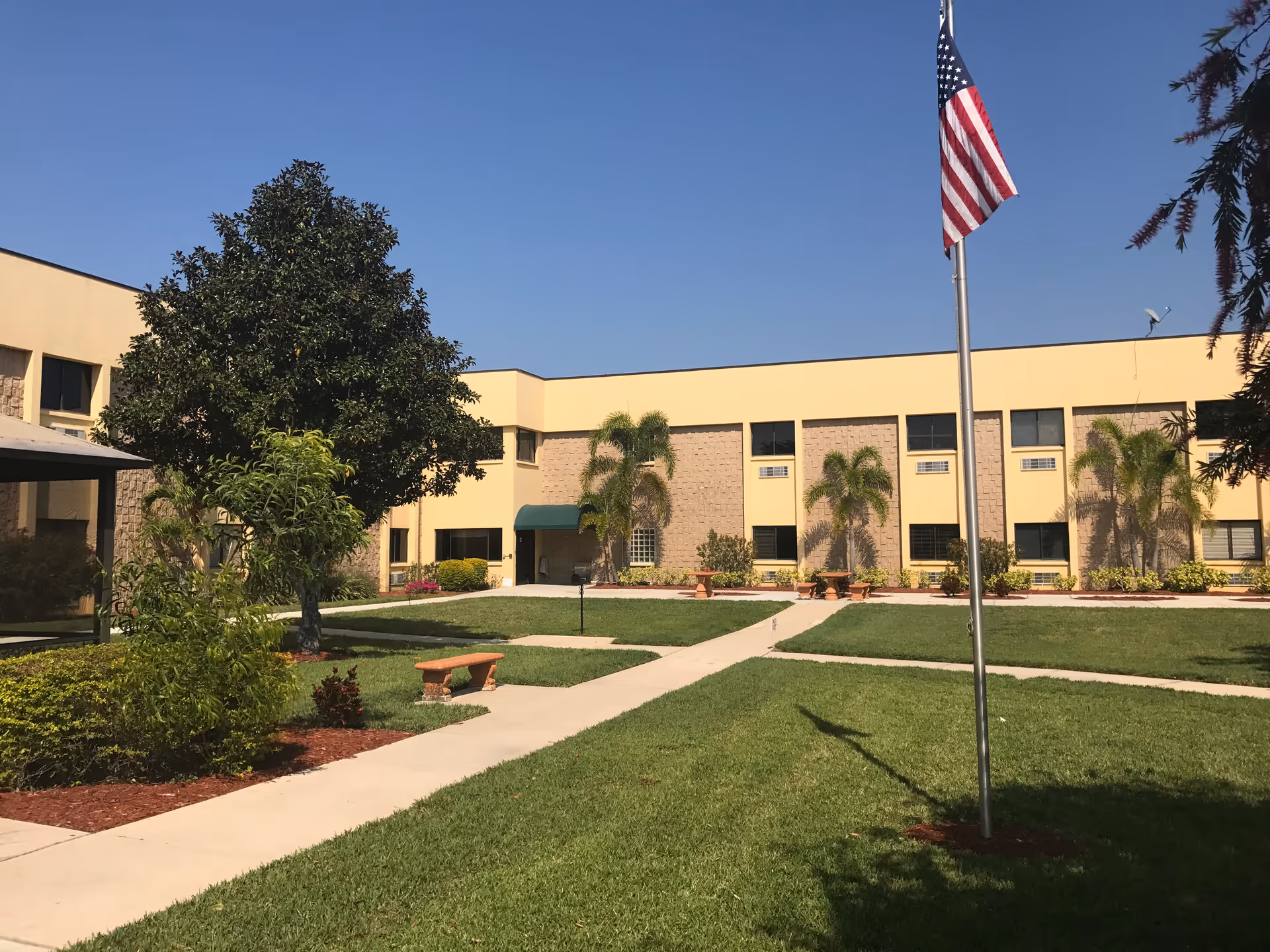 Exterior view of Riviera Palms Rehabilitation Center with lawn, walkways, and a flag.