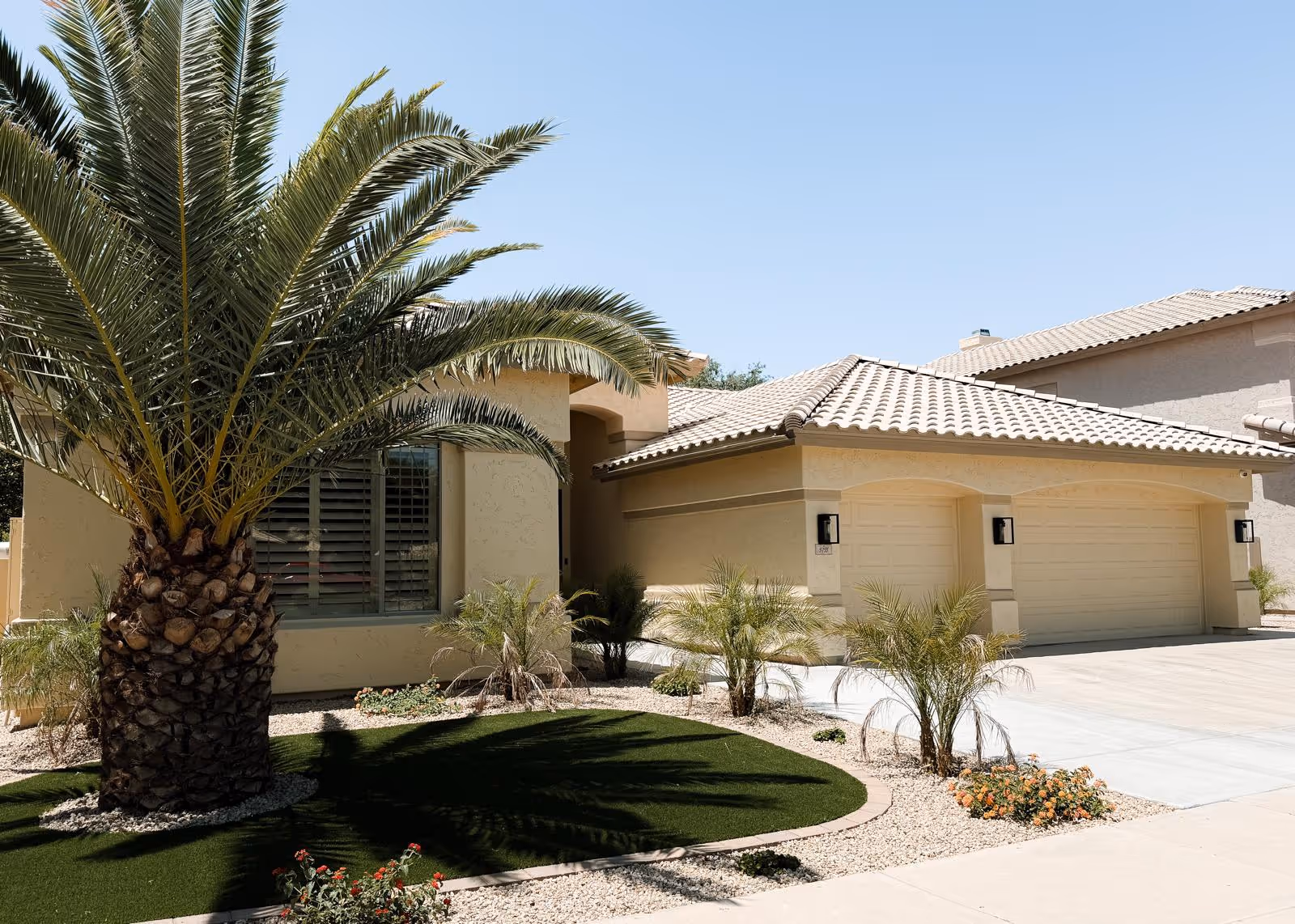 Beige assisted living facility exterior with palm trees, desert landscaping, and a two-car garage.